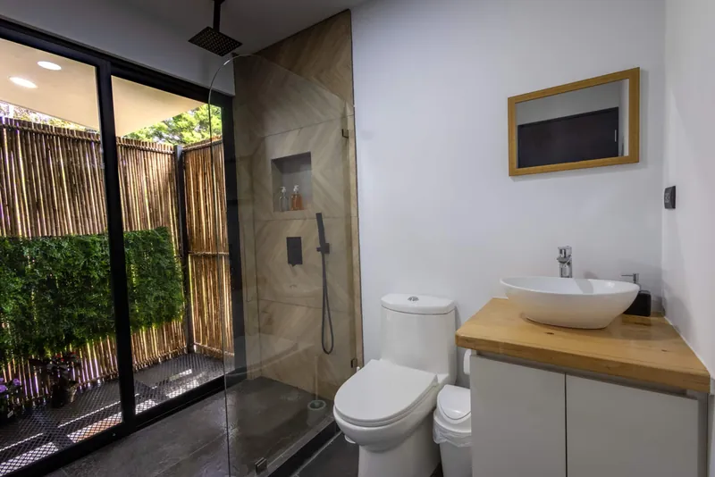 Baño con ducha de vidrio, lavamanos sobre madera y un jardín de bambú afuera
