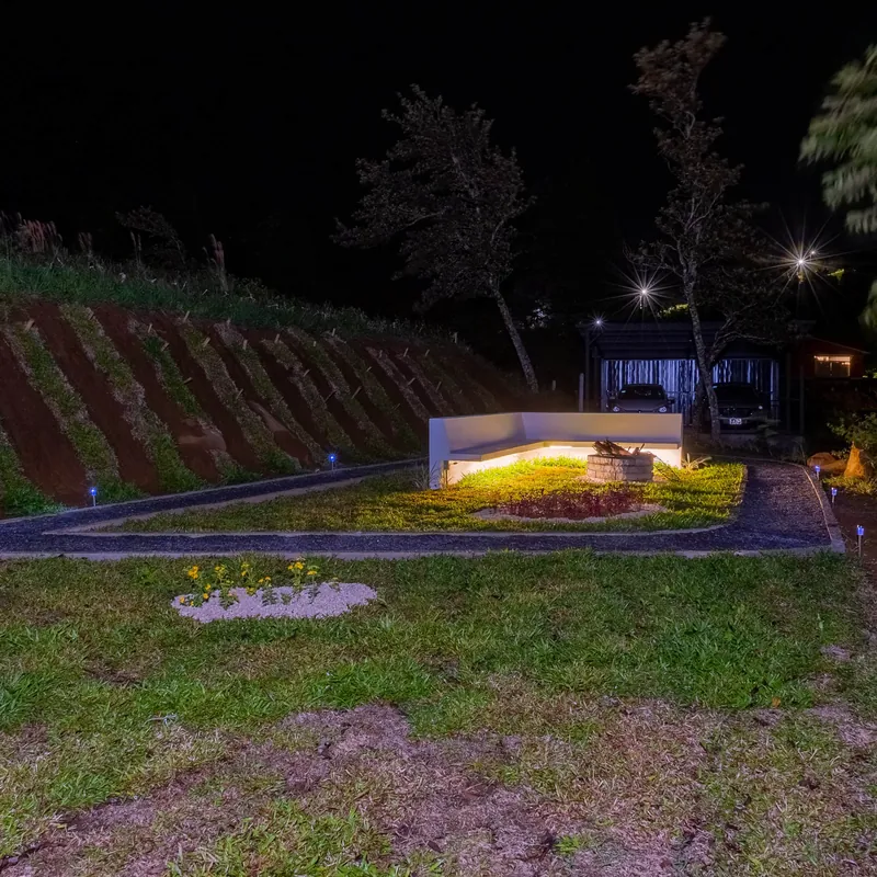 La zona de la fogata iluminada de noche, con la cabaña al fondo